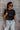 Front view of model wearing the Night Out Sequin Top, which features a sheer black sequin material, a round neck, short sleeves, a black liner, and a back zipper closure