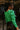 Back side view of model wearing The Lucky Me Sweater features a green knit material, a scoop neck, long sleeves, ruffle detailing at the front sides, and a thick bottom hem.