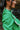 Side view of model wearing The Lucky Me Sweater features a green knit material, a scoop neck, long sleeves, ruffle detailing at the front sides, and a thick bottom hem.