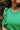 Front view of model wearing The Lucky Me Sweater features a green knit material, a scoop neck, long sleeves, ruffle detailing at the front sides, and a thick bottom hem.