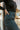 Side view of model wearing The Get In The Groove Pants  features textured dark green fabric with navy stripes, an elastic waist, wide flowy legs, and ankle slits.
