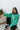 sitting view of model wearing The Best Of Luck Sweatshirt In Green features knit fabric with terrycloth paneling, long raglan sleeves, raw hem details, and a high-low hemline with side slits