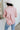 Back view of model wearing the All My Love Faux-Leather Top, which features a pink faux-leather material, a collar neck, a V neckline, long cuffed sleeves, a curved bottom hem, and an oversized fit.