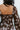 Close-up back view of model wearing the I Like Your Vibe Floral Dress, which features a brown chiffon material, a taupe floral print, a curved neckline, long sleeves, a tier design with ruffles, a smocked back, and a mini length