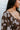 Close-up view of side/top of dress ; model is wearing the I Like Your Vibe Floral Dress, which features a brown chiffon material, a taupe floral print, a curved neckline, long sleeves, a tier design with ruffles, a smocked back, and a mini length