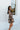 Full body side view of model wearing the I Like Your Vibe Floral Dress, which features a brown chiffon material, a taupe floral print, a curved neckline, long sleeves, a tier design with ruffles, a smocked back, and a mini length