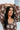 Close-up front view of top of dress; model is wearing the I Like Your Vibe Floral Dress, which features a brown chiffon material, a taupe floral print, a curved neckline, long sleeves, a tier design with ruffles, a smocked back, and a mini length