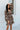 Front view of model wearing the I Like Your Vibe Floral Dress, which features a brown chiffon material, a taupe floral print, a curved neckline, long sleeves, a tier design with ruffles, a smocked back, and a mini length