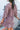 Back view of model wearing the Long Time Coming Dress, which features washed purple fabric, three-quarter sleeves with elastic wrists, a v-neckline, and a flowy tiered body