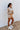 Full body side view of model wearing the Get Cozy Top, which features a sand-colored knit material, a collar neck, a 3/4 button-up front, long sleeves, and a loose fit. Tucked into matching shorts.