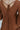 Close-up back view of model wearing the Spice It Up Dress, which features camel-colored fabric, a v-neckline with a cutout, a v-back with a tie, half sleeves, and a flowy fit