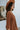Side view of model wearing the Spice It Up Dress, which features camel-colored fabric, a v-neckline with a cutout, a v-back with a tie, half sleeves, and a flowy fit