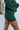 Close-up side view of model wearing the Headed North Shorts, which feature hunter green fabric with horizontal stitched stripes and an elastic waist