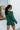 Back view of model wearing the Headed North Top, which features hunter green fabric with horizontal stitched stripes, a round neckline, long sleeves, and a wide cropped fit.