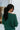 Back view of model wearing the Headed North Top, which features hunter green fabric with horizontal stitched stripes, a round neckline, long sleeves, and a wide cropped fit.