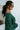 Side view of model wearing the Headed North Top, which features hunter green fabric with horizontal stitched stripes, a round neckline, long sleeves, and a wide cropped fit.