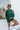 Front view of model wearing the Headed North Top, which features hunter green fabric with horizontal stitched stripes, a round neckline, long sleeves, and a wide cropped fit.