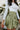 Close-up side view of model wearing the Feeling Lucky Skirt, whcih features green silk fabric with a green lining, a pleated waistband with a smocked back, a front zipper detail, and two front flap pockets