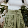 Close-up front view of model wearing the Feeling Lucky Skirt, whcih features green silk fabric with a green lining, a pleated waistband with a smocked back, a front zipper detail, and two front flap pockets