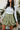 Close-up front view of model wearing the Feeling Lucky Skirt, whcih features green silk fabric with a green lining, a pleated waistband with a smocked back, a front zipper detail, and two front flap pockets