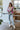 Full body front view of the Full Bloom Cardigan, which features a grey colored knit material, a multi-colored floral pattern, a V neckline, a button-up front, and long sleeves. Cardigan is styled with front tuck