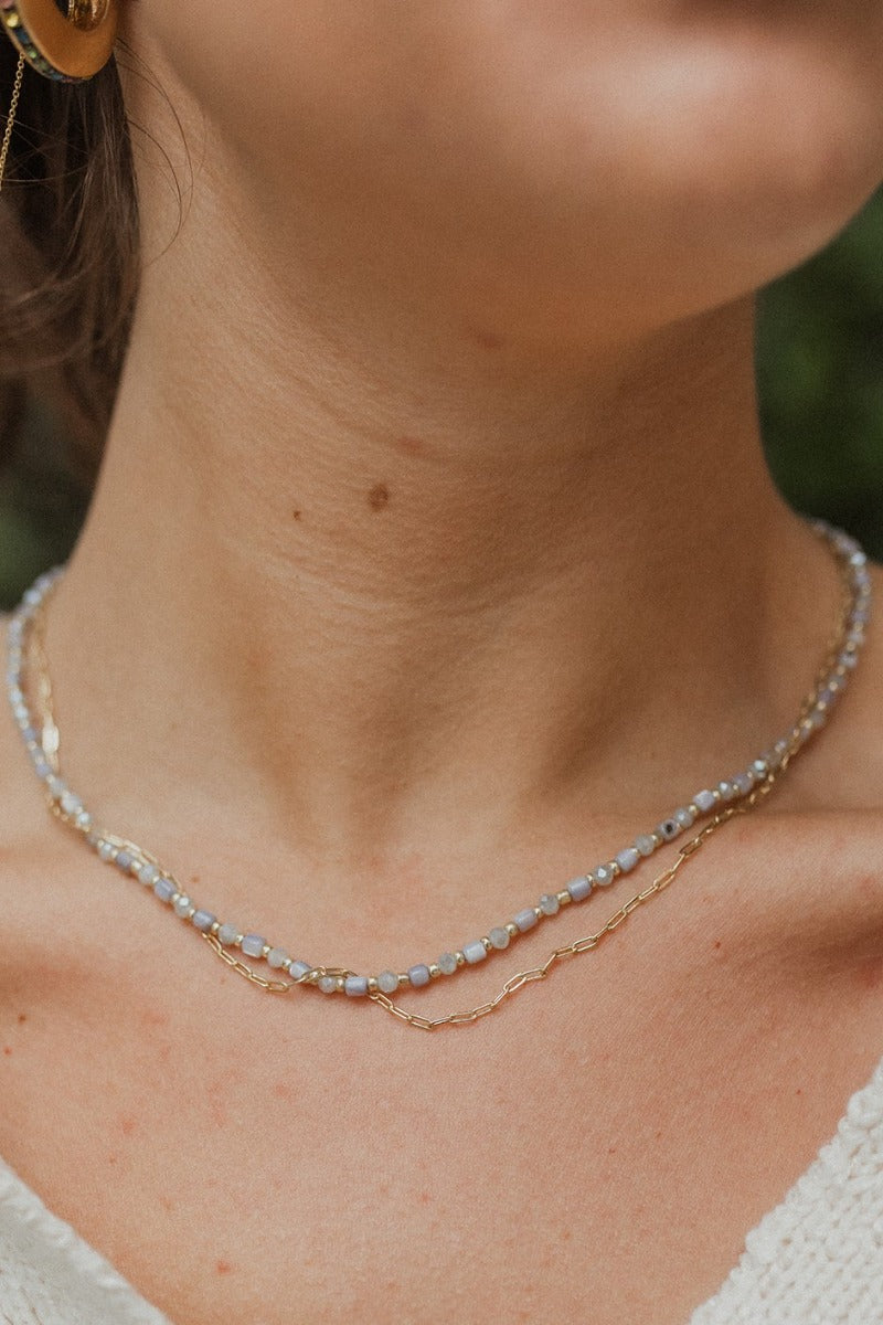 Close view of model wearing the Leap of Faith Necklace, which features double chains: 1 gold link chain and 1 grey beaded chain.