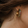 Close-up image of model wearing the Rainbow Road Hoop Earring, which features open gold hoops with a row of multi-colored rhinestones.