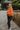 Full body side view of model wearing the Good Morning Teddy Jacket in Rust, that has orange sherpa fabric with corduroy accents, a zip-up front, a front zipper pocket, and long sleeves. Worn unzipped over white top.