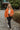 Full body front view of model wearing the Good Morning Teddy Jacket in Rust, that has orange sherpa fabric with corduroy accents, a zip-up front, a front zipper pocket, and long sleeves. Worn unzipped over white top.