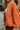 Close-up side view of model wearing the Good Morning Teddy Jacket in Rust, that has orange sherpa fabric with corduroy accents, a zip-up front, a front zipper pocket, and long sleeves. Worn unzipped over white top.