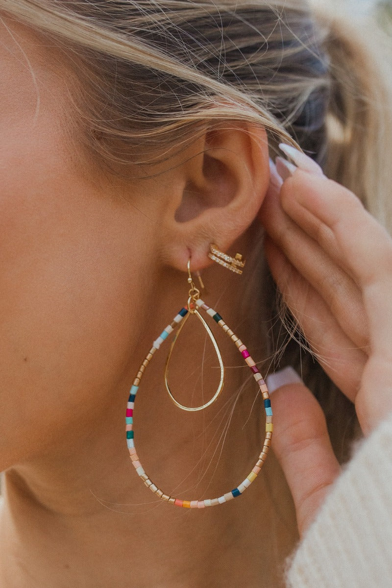 Close-up of model wearing the Lost Without You Earring, which features a large teardrop pendant with multi-colored beads and a smaller gold teardrop pendant.