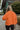 Back view of model wearing the Good Morning Teddy Jacket in Rust, that has orange sherpa fabric with corduroy accents, a zip-up front, a front zipper pocket, and long sleeves. Worn unzipped over white top.