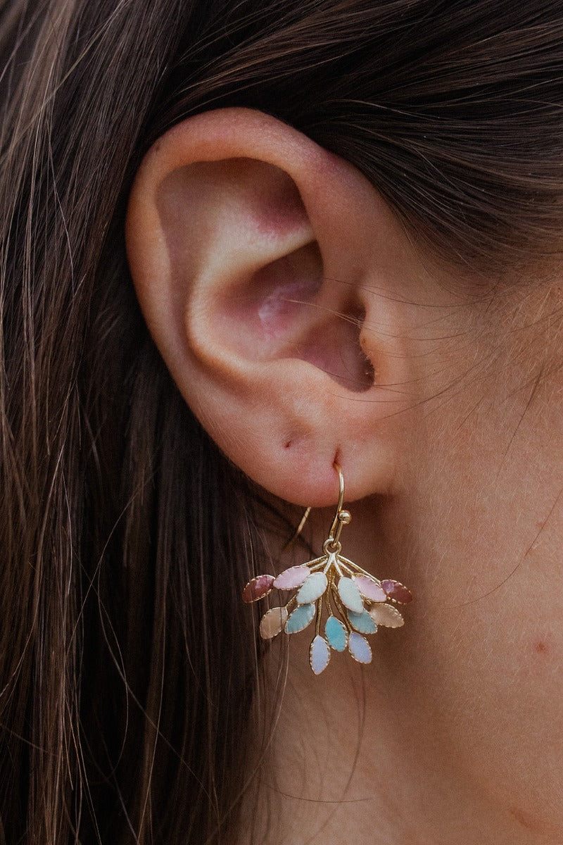 Close-up view of model's ear; model is wearing the Changing Seasons Earrings, which feature gold branches with multi-colored leaves.