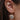 Close-up view of model's ear; model is wearing the Changing Seasons Earrings, which feature gold branches with multi-colored leaves.