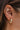 Close-up view of model's ear; model is wearing the Always A Classic Earrings, which feature small gold open hoops with twisted detailing.