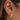 Close-up view of model's ear; model is wearing the Always A Classic Earrings, which feature small gold open hoops with twisted detailing.