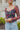 Close up view of model wearing The Slow Down Top which features black mesh fabric with a multi-colored floral print, a lined bodice, a corset front with hook and eye closures, and long sleeves with elastic shoulders.