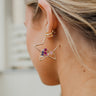Close-up side image of model wearing the Lost In Space Earring, which features gold open star hoops with a pink, navy, white, and gold cluster of rhinestones inside.