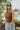 Close front view of model wearing the Take It Easy Bodysuit, which features camel-colored ribbed knit fabric, a round neckline, and a thong bottom with snap closures. Bodysuit is worn with jeans.