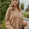 Front view of model wearing the Don't Look Back Hoodie, which features light brown knit fabric, a henley neckline with tortoise buttons, a hood with drawstrings, a rounded hemline, and long sleeves with ribbed wrists