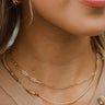 Close view of model wearing the Free To Be Necklace, which features double strands: 1 shorter gold link chain, and 1 strand with beige, brown, and gold beads.