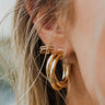 Close view of model wearing the What A Twist Hoop Earrings, which feature open gold twisted hoops.
