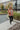 Full body view of model wearing The Keep Me Warm Quilted Jacket which features quilted terracotta-colored fabric, two large front pockets, and a snap-up front with a collared neckline.