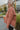 Side view of model wearing The Keep Me Warm Quilted Jacket which features quilted terracotta-colored fabric, two large front pockets, and a snap-up front with a collared neckline.