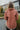 Back view of model wearing The Keep Me Warm Quilted Jacket which features quilted terracotta-colored fabric, two large front pockets, and a snap-up front with a collared neckline.