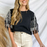 Front view of model wearing the Life Of The Party Top, that has black fabric, a round neckline, and short sleeves with black and silver sequin tassels