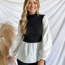 Front view of model wearing the Kendall Two-In-One Top features white oxford fabric, an attached black knit fabric overlay, a high neckline, and long balloon sleeves.