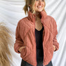 Front view of model wearing the Emerson Corduroy Puffer Jacket in Terracotta that has corduroy fabric, diamond-shaped puffer stitching, a monochromatic zipper with a high neck, two front pockets, a drawstring hem, and long sleeves.