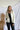Front view of model wearing the Yosemite Puffer Jacket that has ivory puffer fabric, two front pockets, black zipper details, a zip-up front, and a hood. Worn over black top.