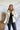 Front view of model wearing the Yosemite Puffer Jacket that has ivory puffer fabric, two front pockets, black zipper details, a zip-up front, and a hood. Worn over black top.